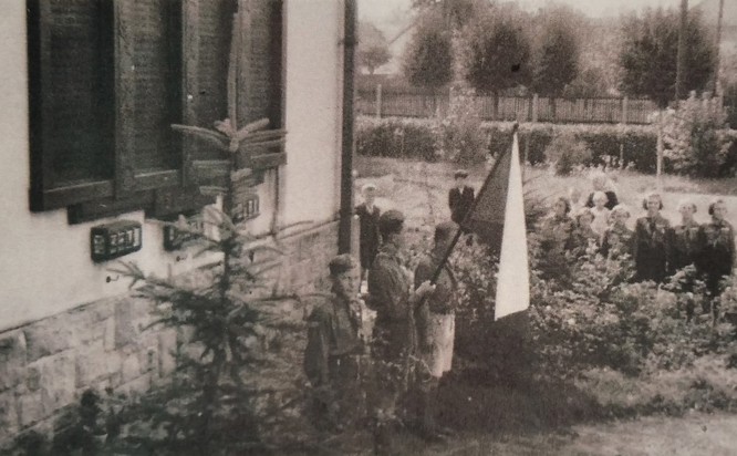 Zobrazit obrázek: Vzpomínková akce u pamětní desky padlých v první světové válce. Pod ní jsou ještě patrné tři skříňky na prsť z bojišť